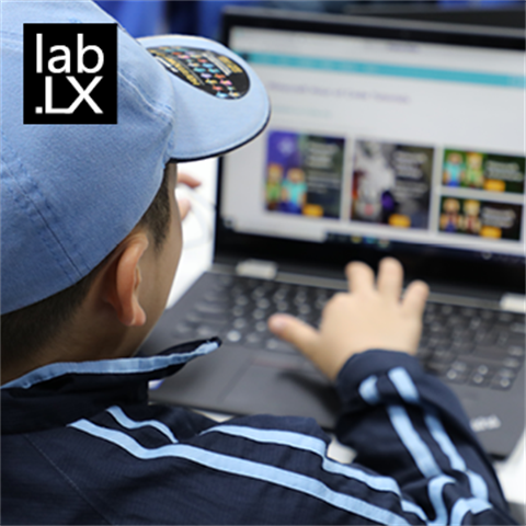 A boy is wearing a blue hat and navy jacket playing on his laptop