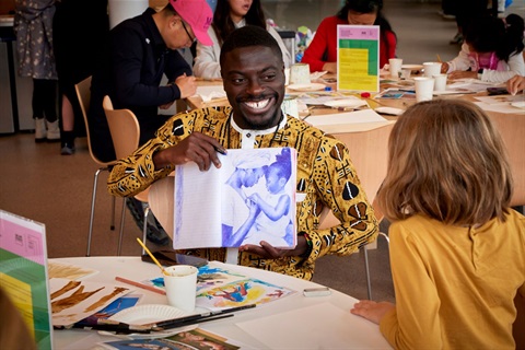  Artist Emmanuel Asante smiles while holding a draw to show to a kid.
