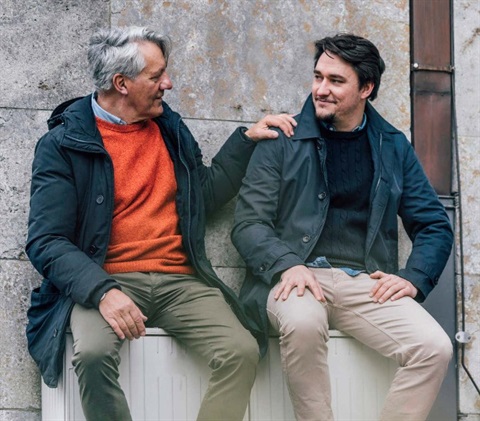 Older man putting hand on the should of a younger man who he is sitting next to