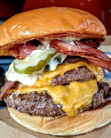 Huge burger stuffed with meat, cheese, bacon, pickles and sauce