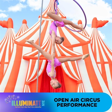 Two young open air circus performers hanging upside down in front of big top