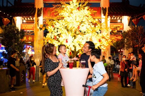 A family of four laughing around a small table at night in front of a lit up decorated tree at Freedom Plaza