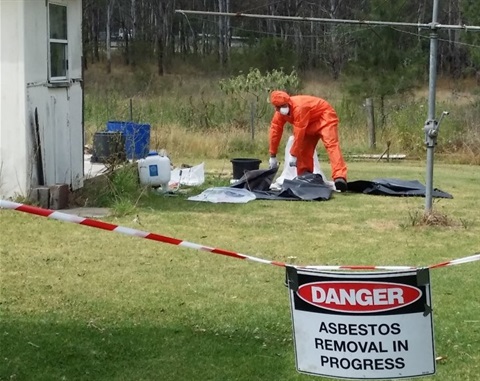 Asbestos being removed from worksite by person in orange safety suit