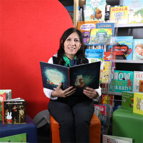 Image of female librarian smiling at the camera while reading a picture book