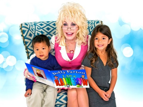Dolly Parton posing with a young boy and girl on an armchair reading a book 