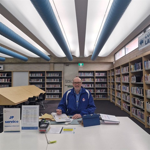 A library staff sitting in a staff desk in the library with a JP service sign.