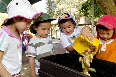 Children pouring food waste from lunch box into compost bin