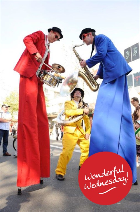 Hi Life Horns stilt walkers dressed in red, yellow and blue suits while playing the drums, sousaphone and saxophone