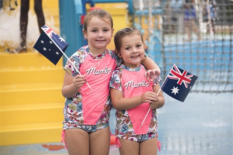 Two young girls smiling and posing while waving Australian flags at Aquatopia 