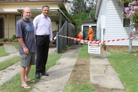 Mayor Frank Carbone smiling and posing with a man next to safety tape and sign saying Danger Removal of Asbestos in progress