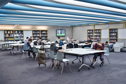 Group of people reading newspapers and looking at their phones while sitting around tables