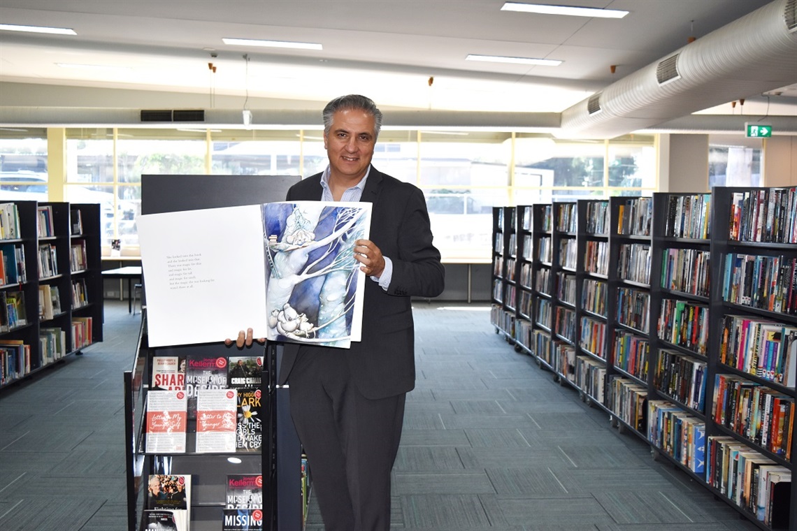 Mayor Frank Carbone smiling and posing with a book at Wetherill Park Library