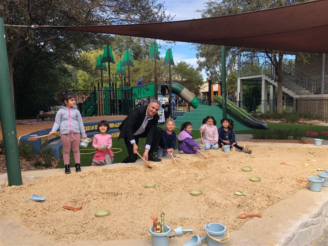Mayor Frank Carbone and young girls smiling and posing at a sand pit in Fairfield Preschool