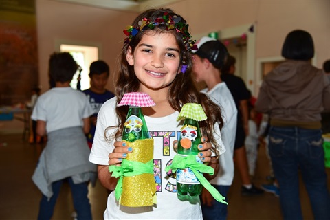 Young girl smiling and posing while holding two recycled bottle crafts 