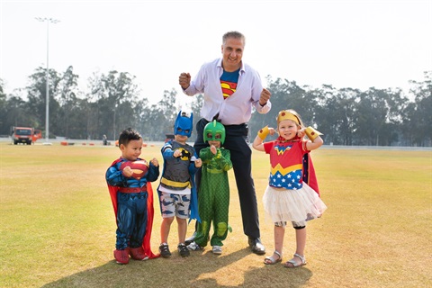 Mayor Frank Carbone dressed as Superman smiling and posing with young children wearing superhero costumes