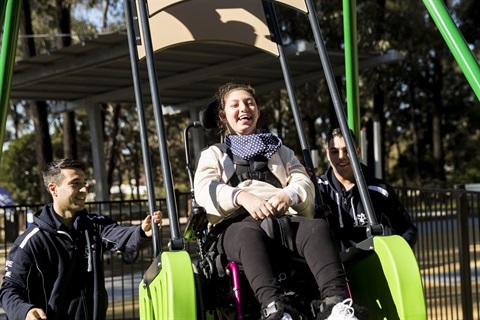 Girl in wheelchair riding on all abilities swing at the opening of Deerbush Park