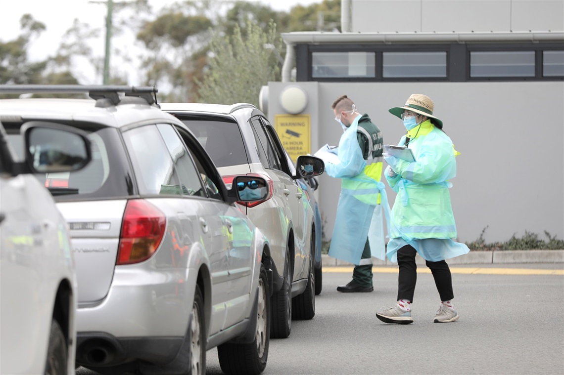 Cars lined up and people in masks and gowns 