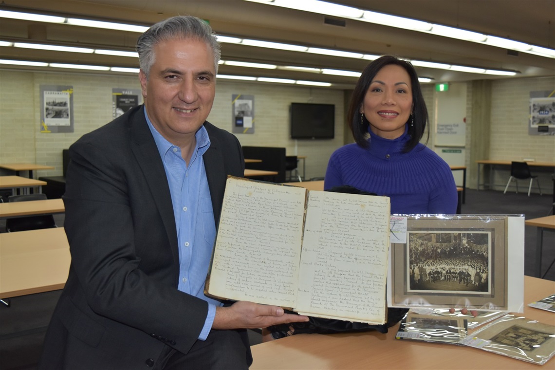 Mayor Frank Carbone and Councillor Dai Le smiling and posing with the earliest surviving records of Council minutes at Whitlam Library