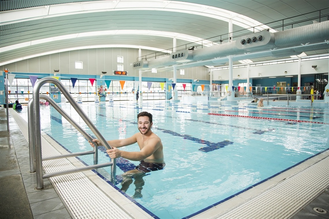 Young man smiling while holding on the pool ladder at Prairiewood Leisure Centre