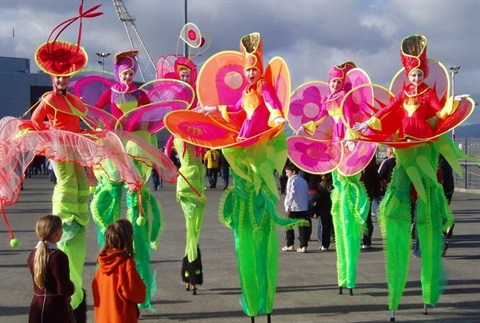 Street entertainers wearing colourful pink and green costumes walking on stilts