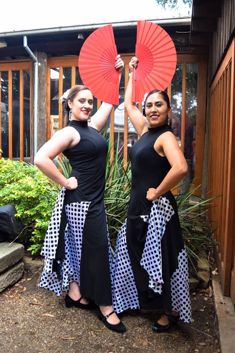Two women wearing black and white costumes while smiling and posing with red fans