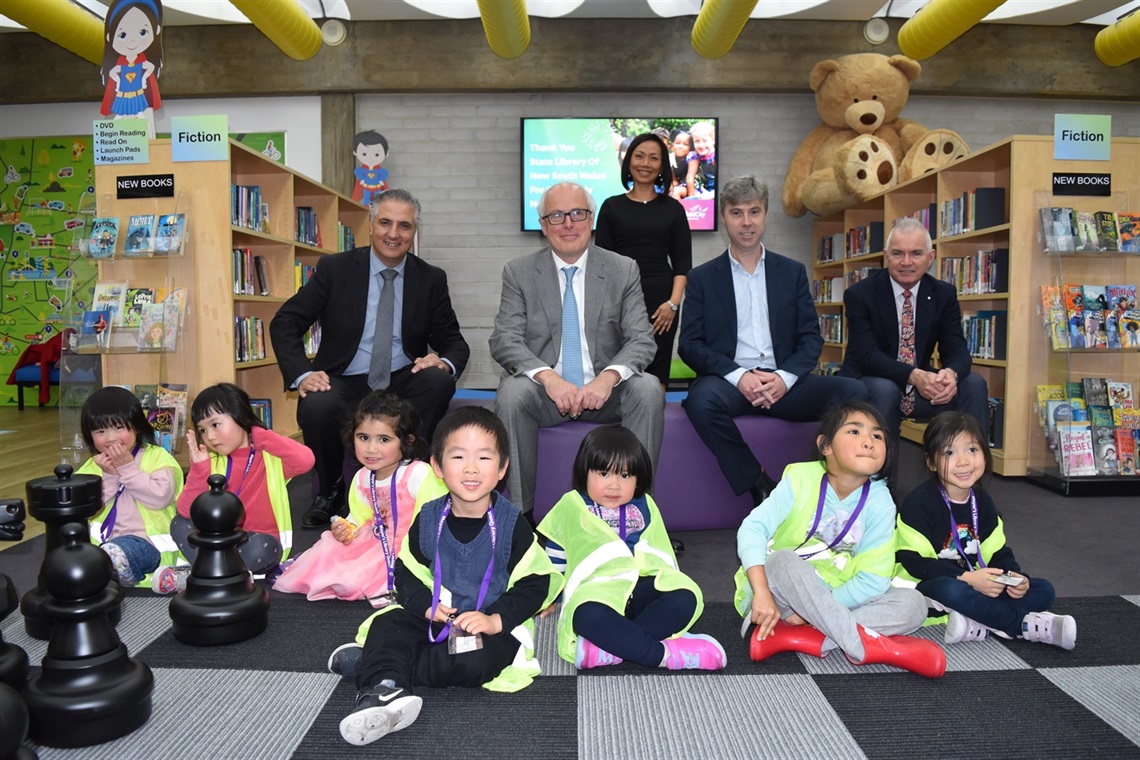 Mayor Frank Carbone, State Librarian John Vallance, Councillor Dai Le and City Manager Alan Young smiling and posing with young children in the Whitlam Library's children's area