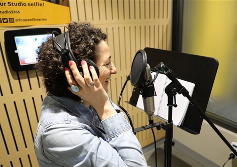 Woman wearing and holding onto headphones while talking into a microphone 