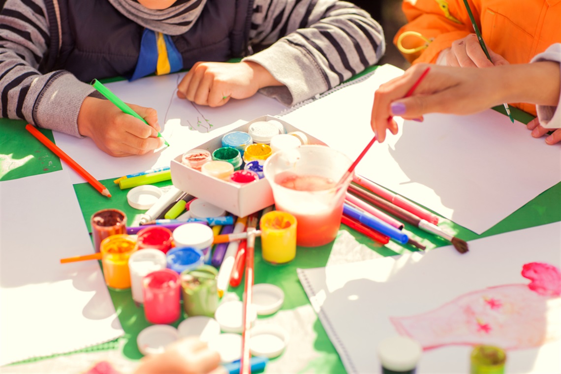 Group of children sitting around a green table, using colourful pencils, markers and paint