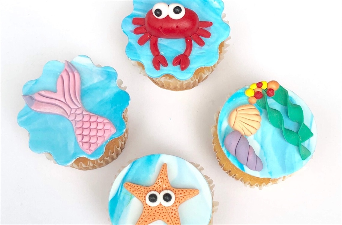 Four blue and white cupcakes with sea life decorations on top of each cupcake