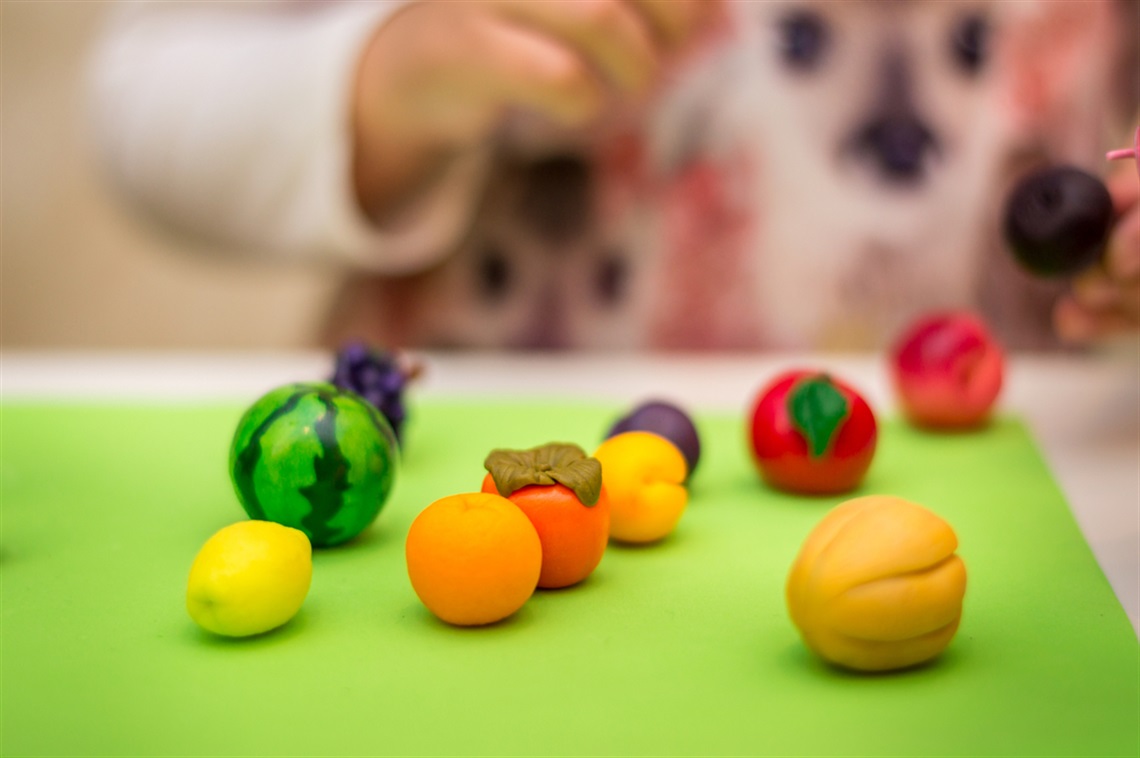 Close up of child moulding miniature polymer fruit sculptures 