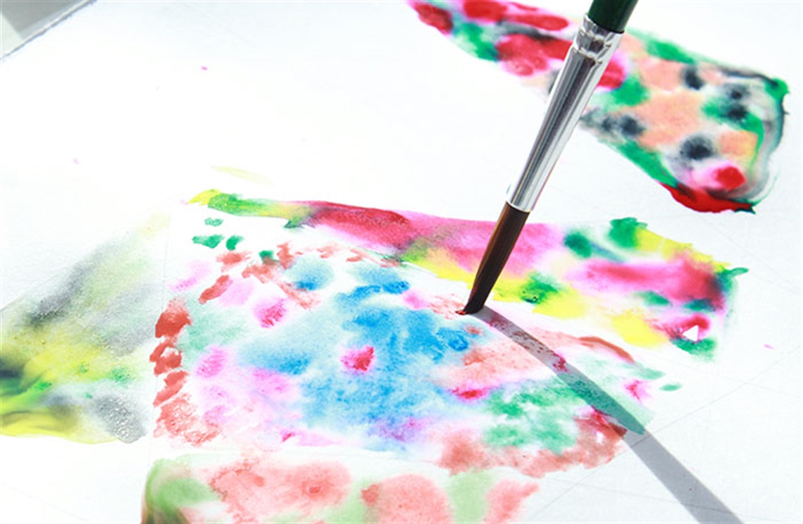 Paint brush making small strokes to colourful water colour painting 
