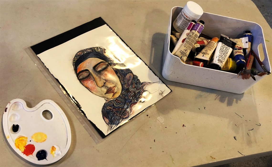 Portrait painting sitting on a table next to a tub of paint tubes and palette 