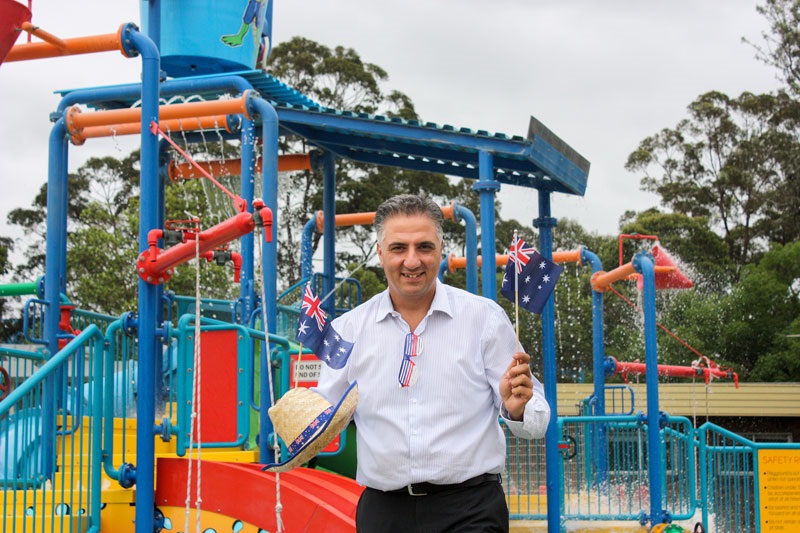 Mayor Frank Carbone smiling and posing with Australian flags in front of Aqua Play Water Park at Fairfield Leisure Centre
