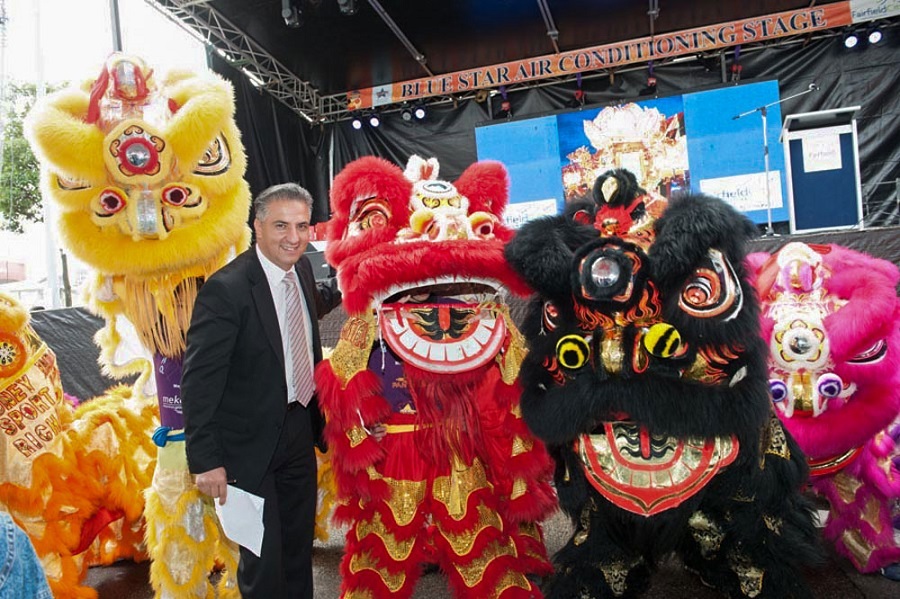Mayor Frank Carbone smiling and posing with colourful lion dancing puppets in front of the Blue Star Air Conditioning Stage at Cabramatta Moon Festival