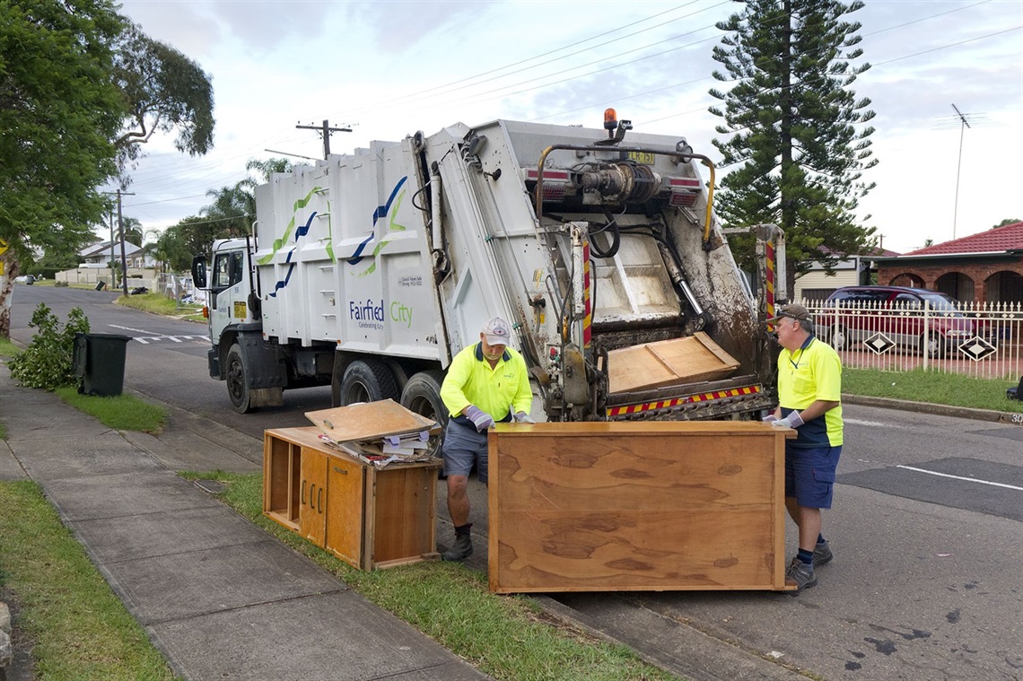 Garbage collectors loading disposed wooden furniture onto a garbage truck