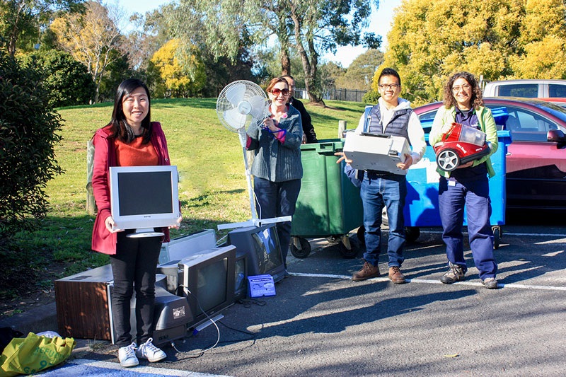 Group of people smiling and posing, holding old and disposed home appliances 