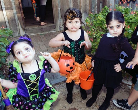 Young girls dressed in Halloween costumes while holding Jack O Lantern buckets