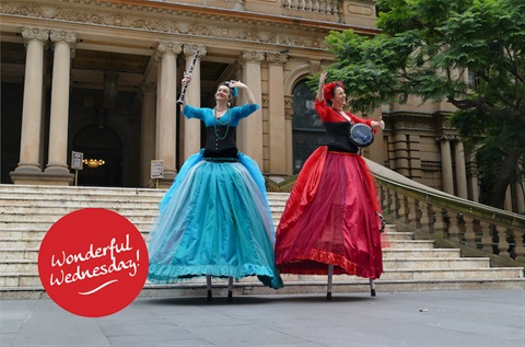 Musical Maidens on stilts wearing blue and red gowns while holding musical instruments
