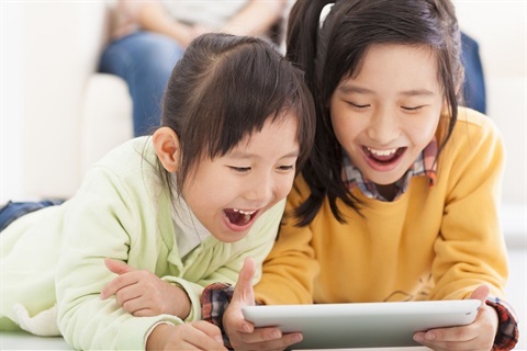 Two young girls smiling and laughing while looking at tablet screen