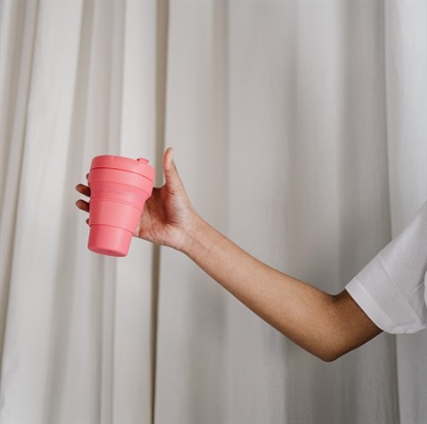 Person holding pink reusable coffee keep cup 