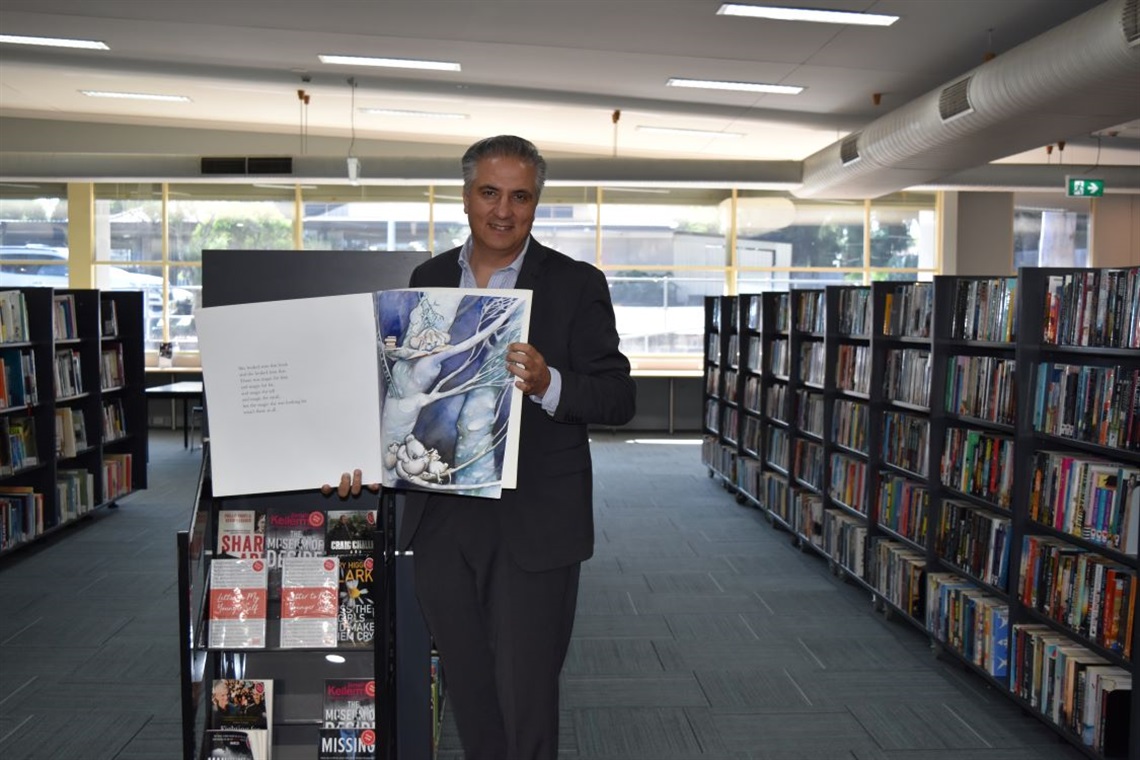 Mayor Frank Carbone smiling and posing with children's story book at the Wetherill Park Library 