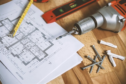 Construction tools like drills and measuring tape lying on table beside a building blueprint
