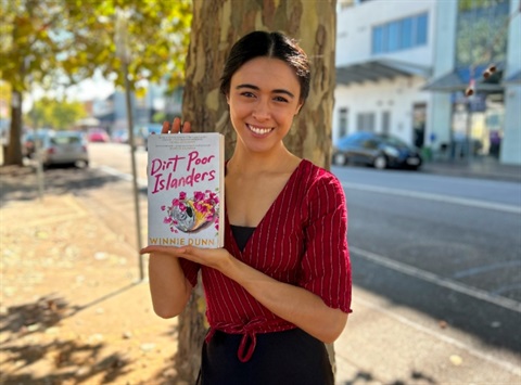 Author Winnie Dunn holding her novel Dirt Poor Islanders.