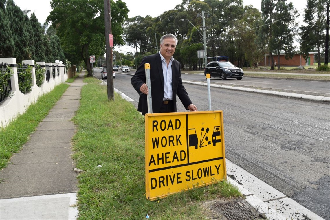Mayor Frank Carbone smiling and posing with sign saying 'Road Work Ahead, Drive Slowly' 