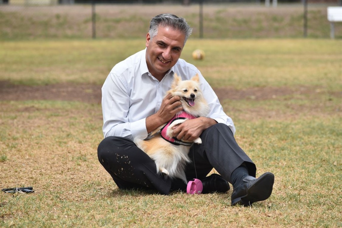 Mayor Frank Carbone smiling and posing with a dog while sitting on the grass at a park