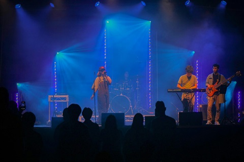 A band performs on stage, illuminated by vibrant blue lights, creating an energetic atmosphere.