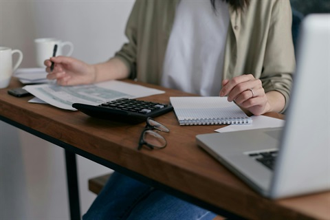A woman sits at a desk with a laptop open and a cup of coffee beside her, focused on her work.