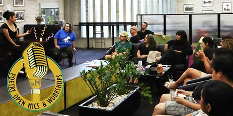 A diverse group of people seated around a table, each with a microphone, engaged in discussion or a meeting.