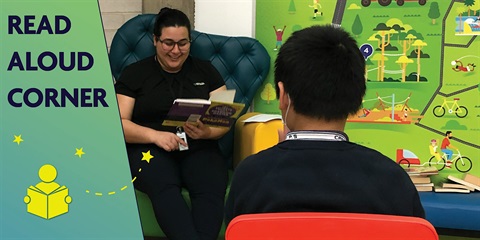 A student engages another student with a book in a corner, fostering a nurturing and imaginative reading experience.
