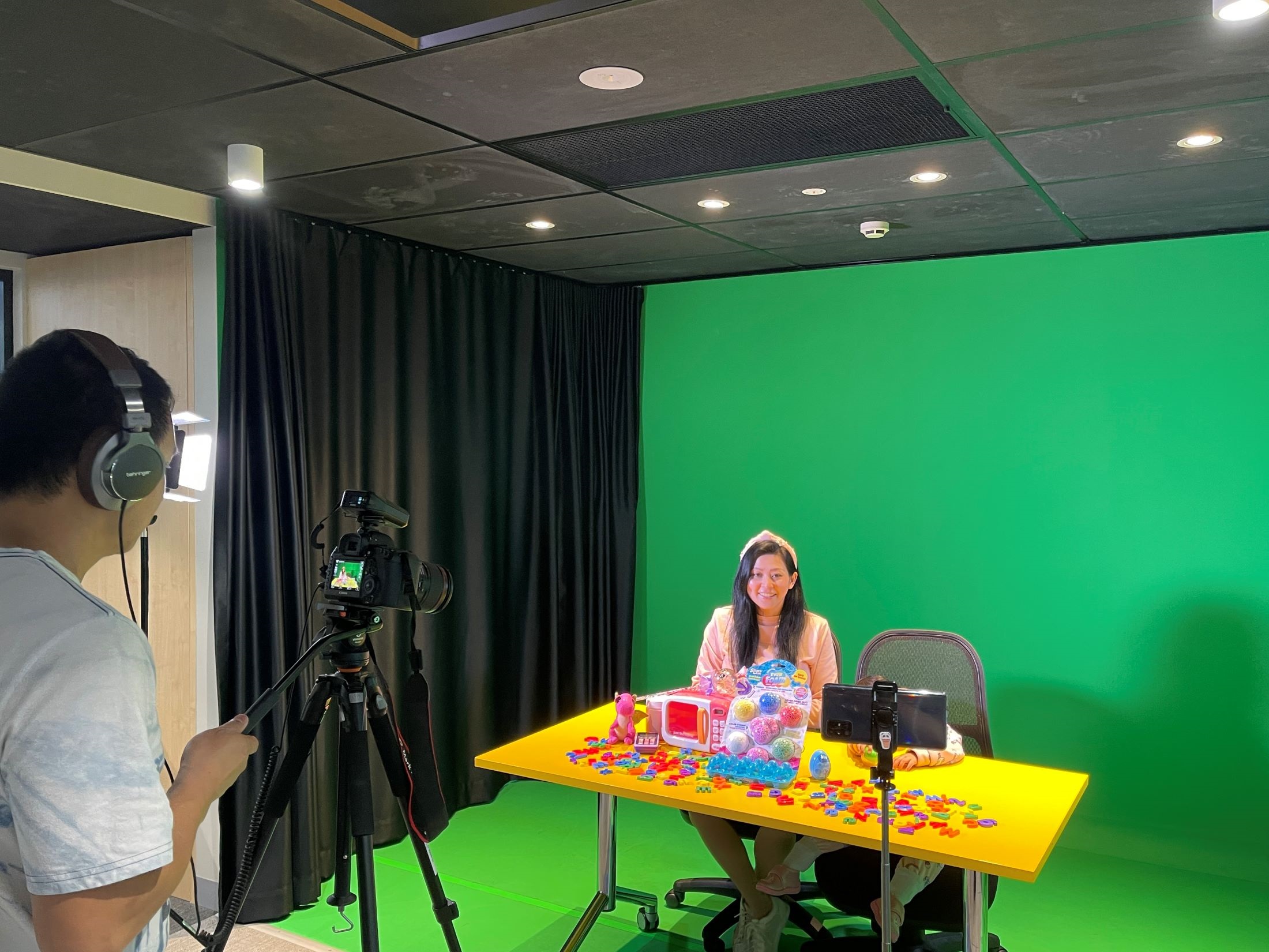 Man-filming-lady-on-camera-in-front-of-green-screen